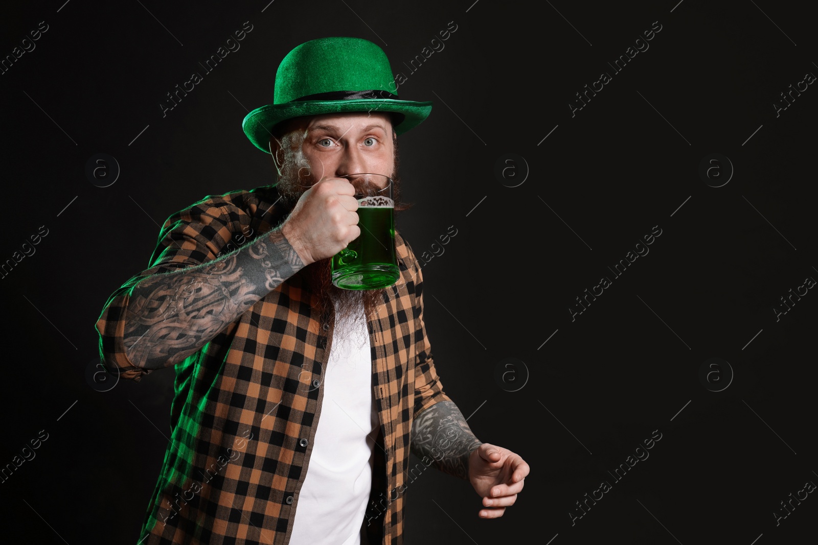 Photo of Bearded man drinking green beer on black background, space for text. St. Patrick's Day celebration