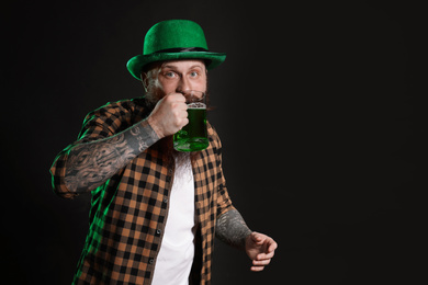 Photo of Bearded man drinking green beer on black background, space for text. St. Patrick's Day celebration
