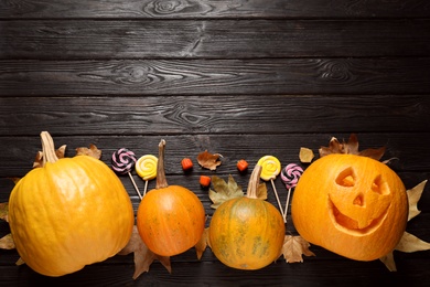 Photo of Flat lay composition with pumpkin head Jack lantern and Halloween treats on black wooden background. Space for text