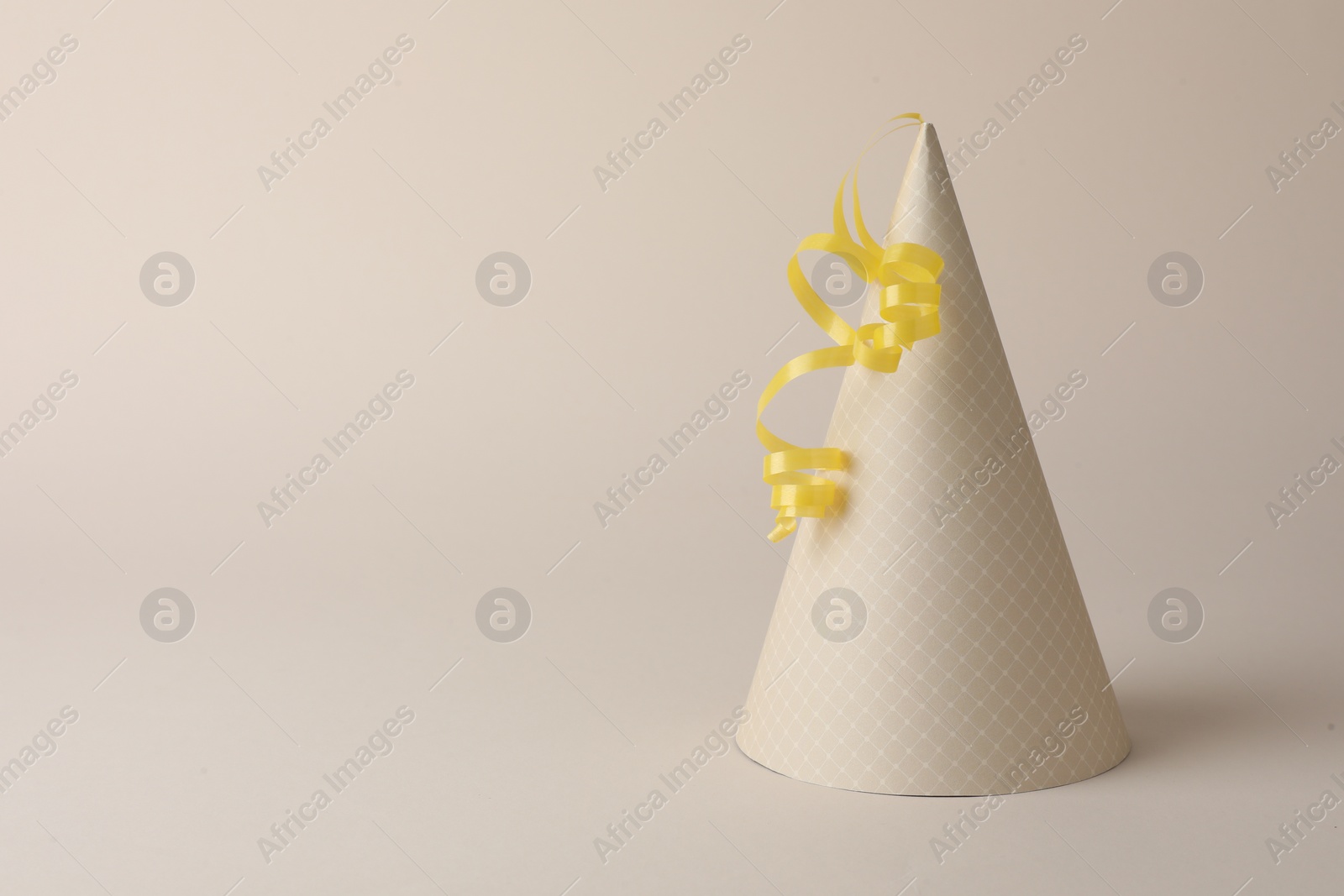 Photo of One beautiful party hat with serpentine streamer on beige background. Space for text