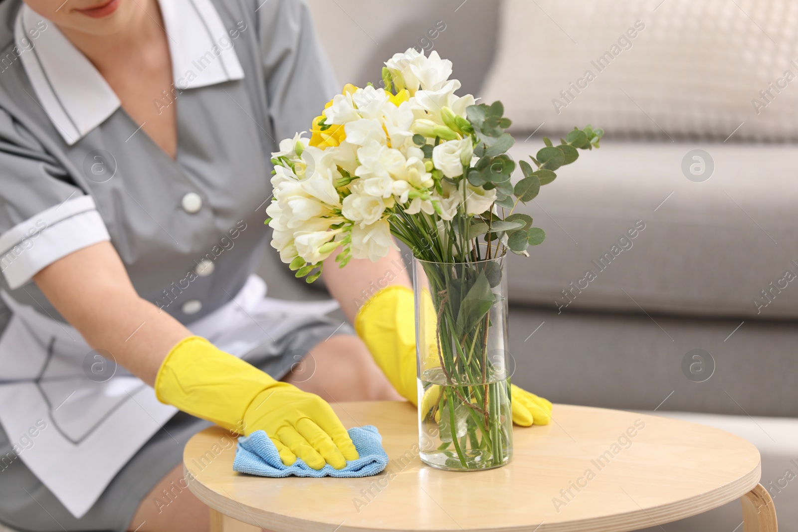 Photo of Young chambermaid wiping dust from wooden table in hotel room, closeup