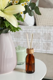 Photo of Aromatic reed air freshener and vase with bouquet on white table in bedroom