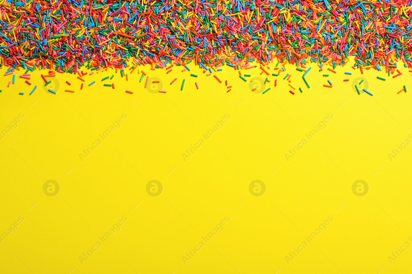 Photo of Bright colorful sprinkles on yellow background, flat lay with space for text. Confectionery decor