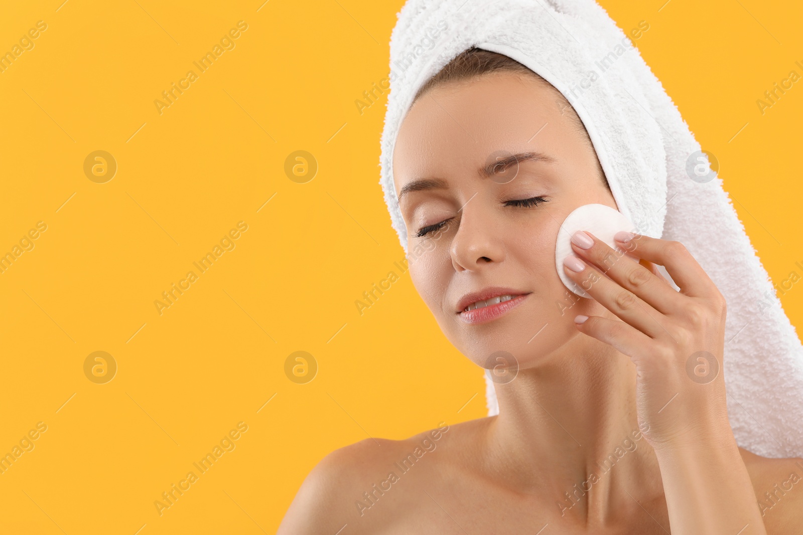 Photo of Beautiful woman removing makeup with cotton pad on yellow background, closeup. Space for text