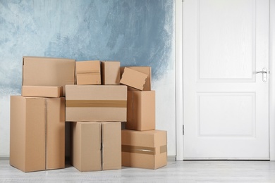 Photo of Pile of cardboard boxes near color wall indoors. Space for text