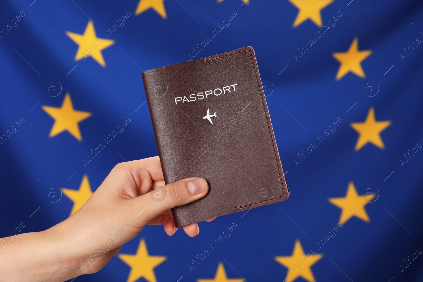 Photo of Woman holding passport against flag of European Union, closeup