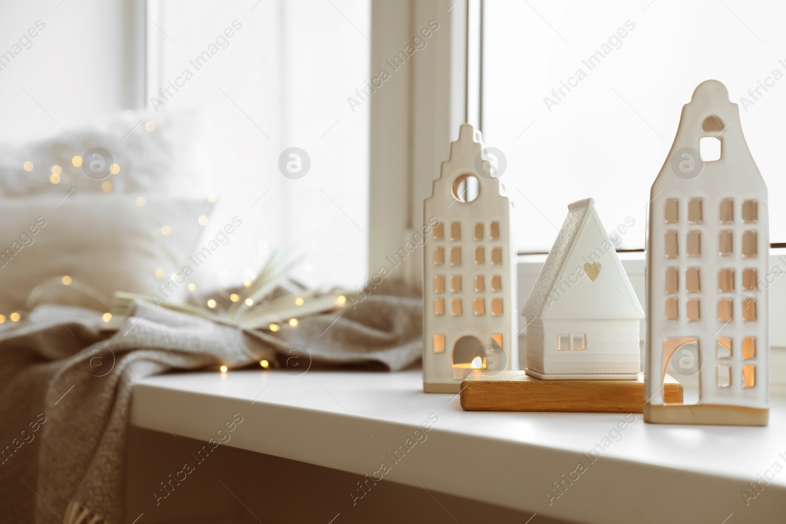 Photo of Beautiful house shaped candle holders and festive lights on windowsill indoors, space for text