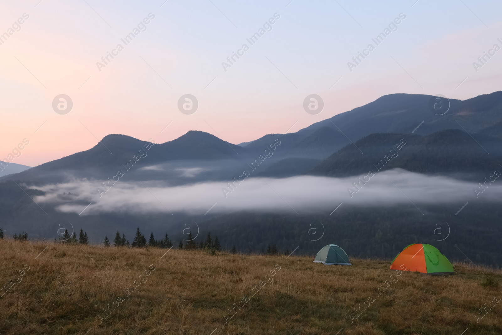 Photo of Picturesque view of mountain landscape with fog and camping tents in early morning