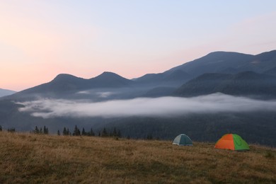 Picturesque view of mountain landscape with fog and camping tents in early morning