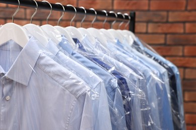 Dry-cleaning service. Many different clothes in plastic bags hanging on rack against brick wall, closeup