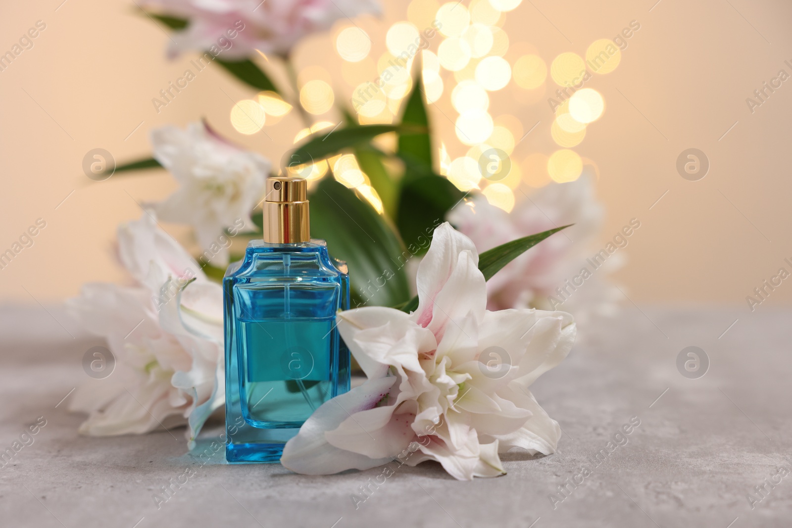 Photo of Bottle of perfume and beautiful lily flowers on table against beige background with blurred lights, closeup