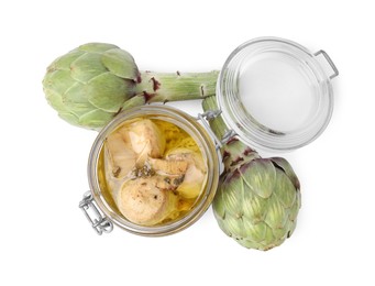 Open jar of delicious artichokes pickled in olive oil and fresh vegetables on white background, top view