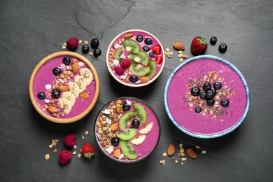 Photo of Acai smoothie bowls with granola and fruits on black table, flat lay