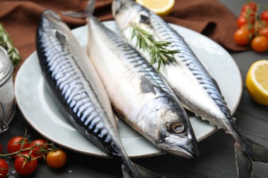 Photo of Raw mackerel, tomatoes and rosemary on black wooden table, closeup