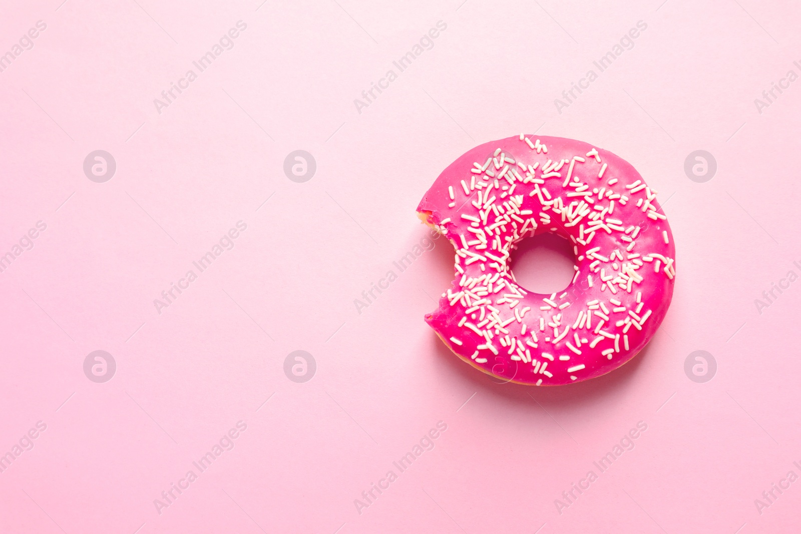 Photo of Delicious bitten doughnut with sprinkles on color background, top view