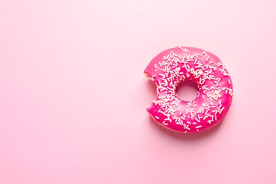 Photo of Delicious bitten doughnut with sprinkles on color background, top view