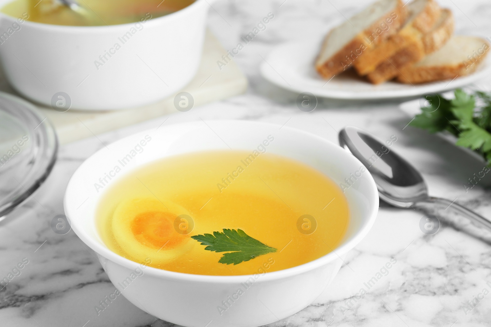 Photo of Delicious bouillon with egg and parsley in bowl on white marble table