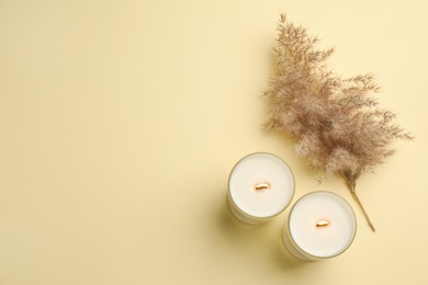 Photo of Burning soy candles and dry reed on beige background, flat lay. Space for text