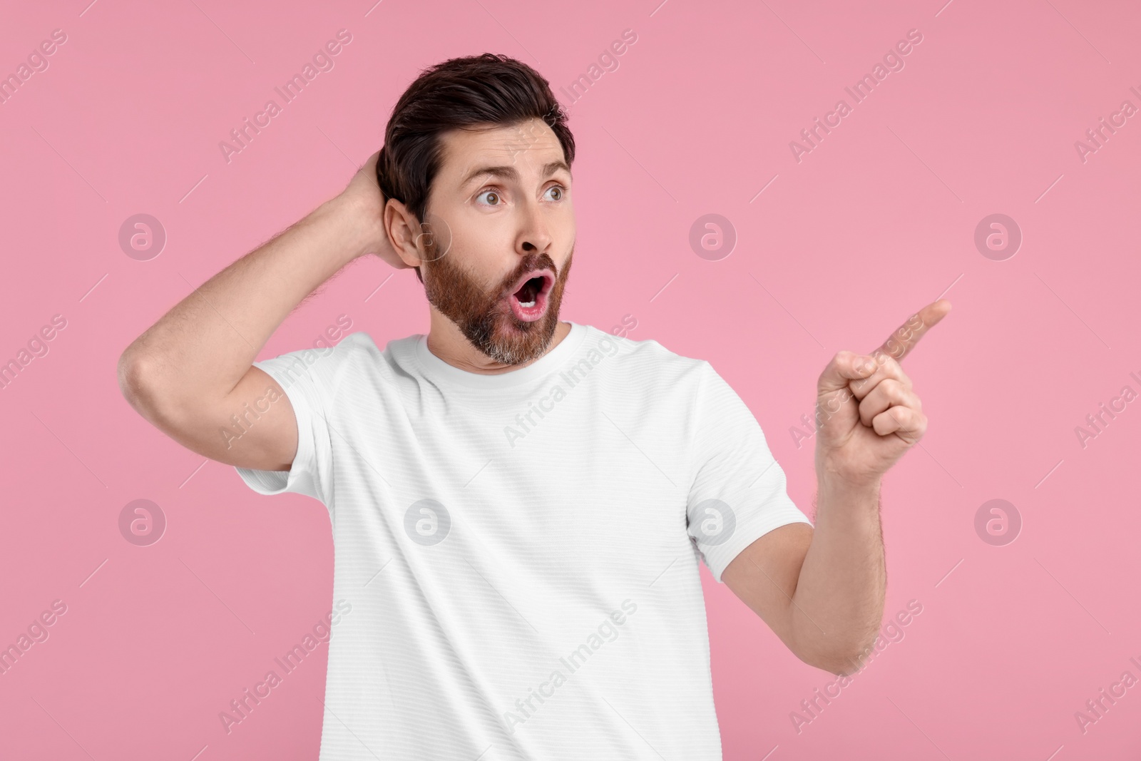 Photo of Surprised man pointing at something on pink background