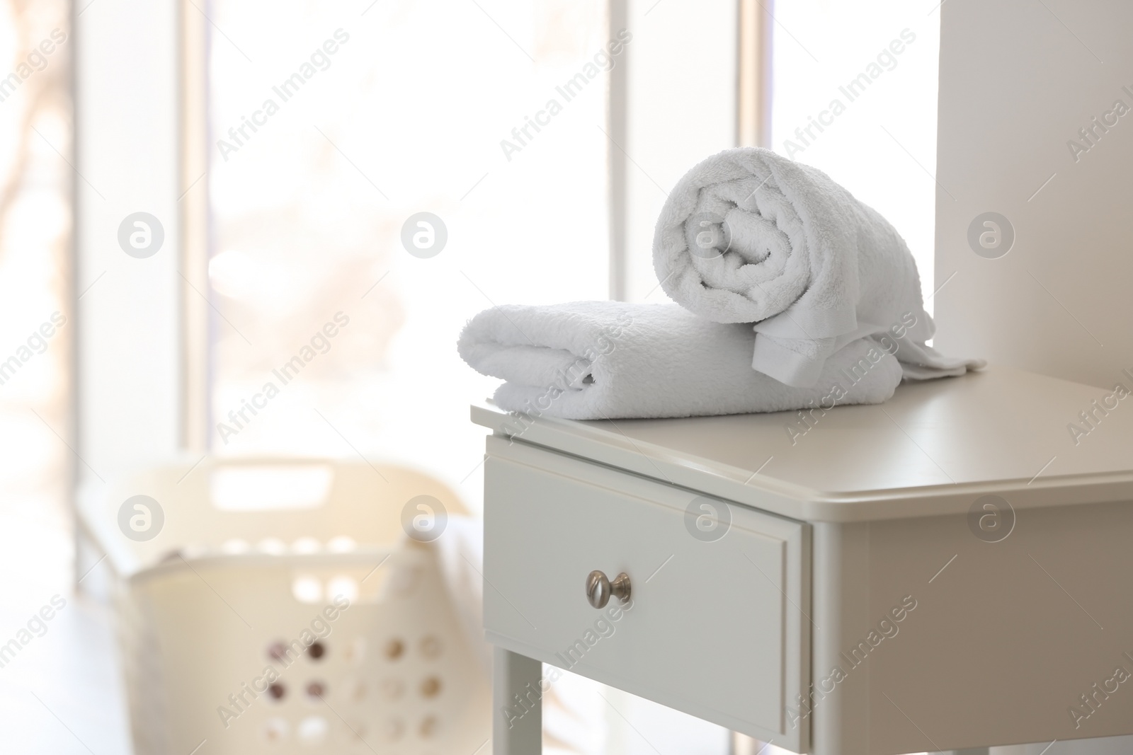 Photo of Clean towels on table and blurred laundry basket indoors