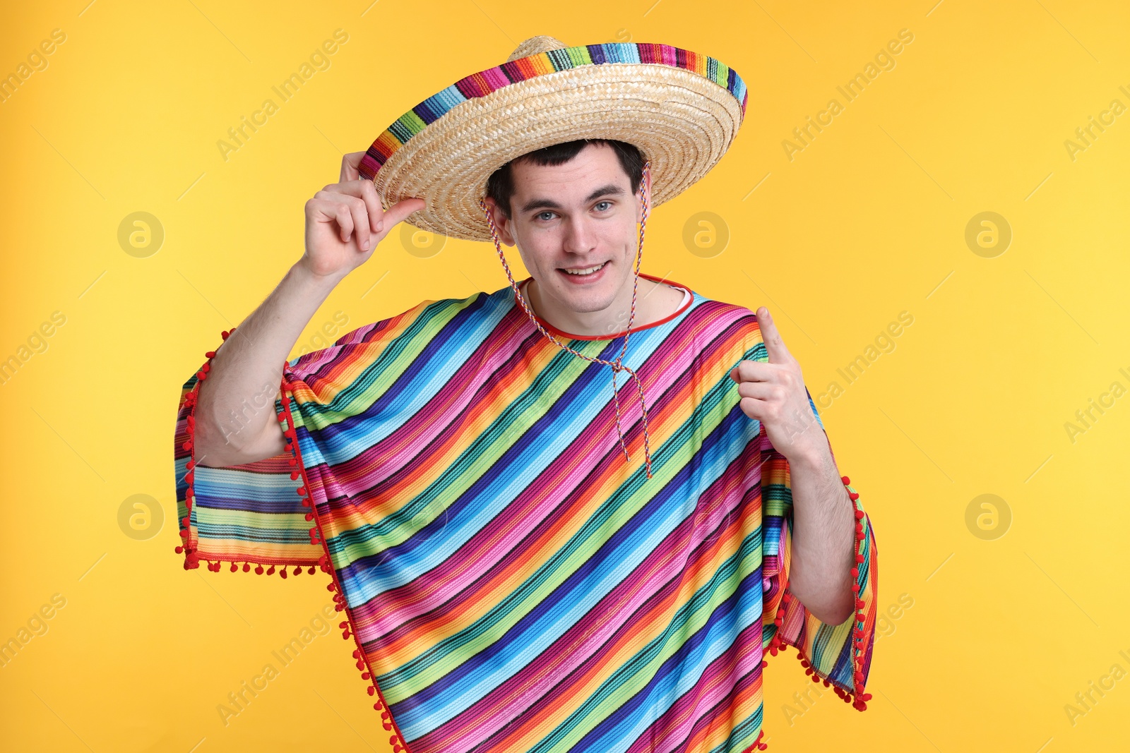 Photo of Young man in Mexican sombrero hat and poncho on yellow background