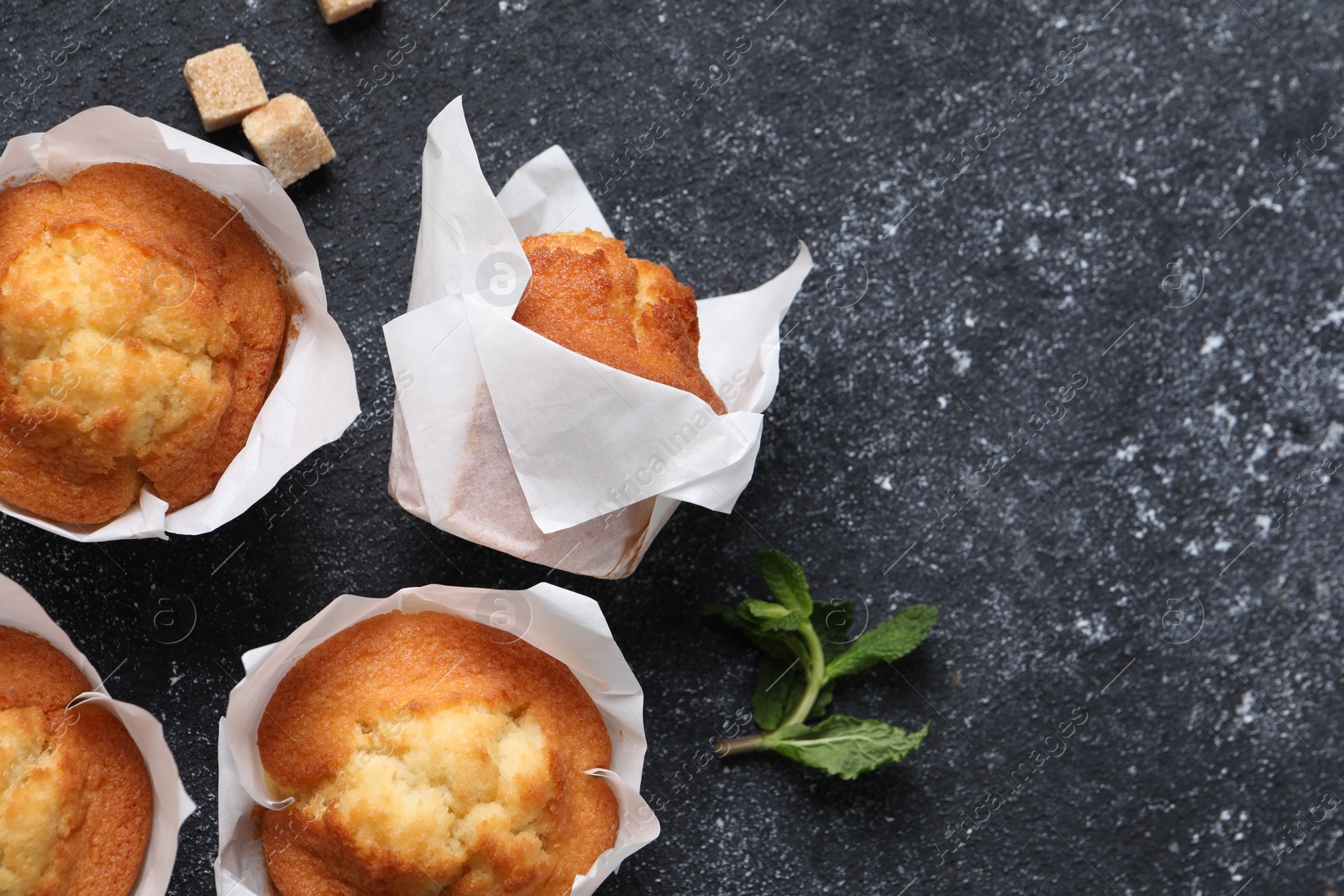 Photo of Delicious sweet muffins and brown sugar on black textured table, flat lay. Space for text