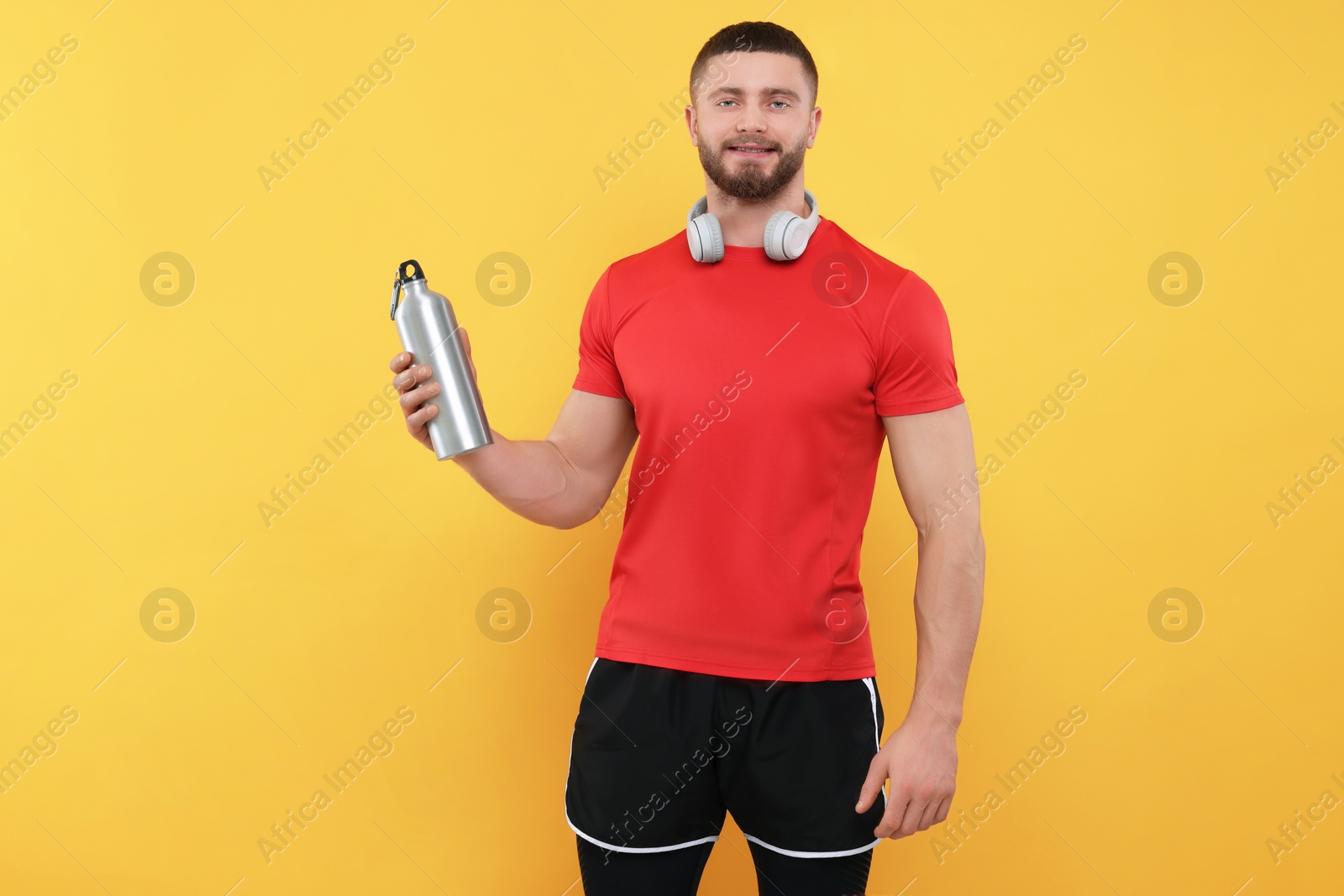 Photo of Handsome man with headphones and thermo bottle on yellow background, space for text