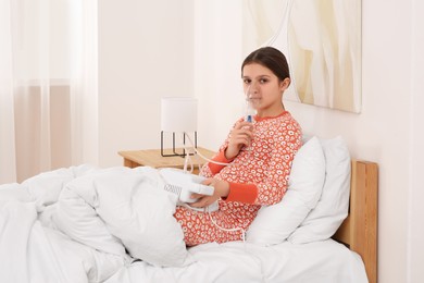 Cute girl using nebulizer for inhalation on bed at home