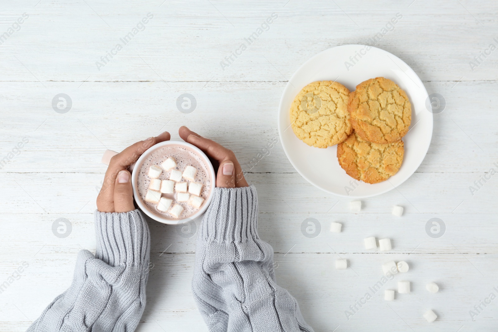 Photo of Woman holding cup of delicious cocoa drink at white wooden table, top view