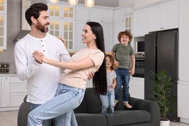 Photo of Happy family having fun at home. Couple dancing while children jumping on sofa