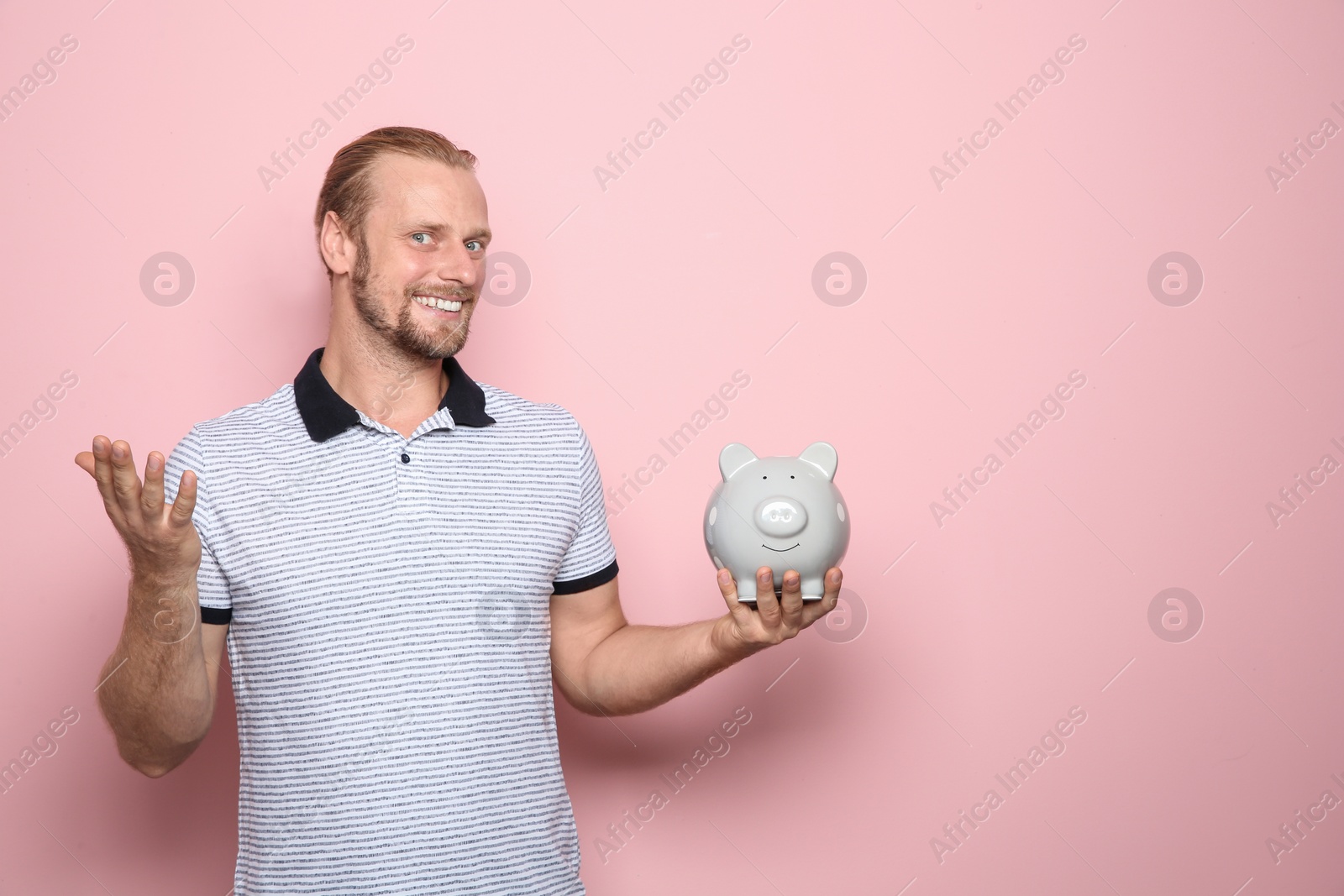 Photo of Happy man with piggy bank on color background. Space for text