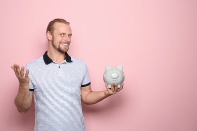 Happy man with piggy bank on color background. Space for text