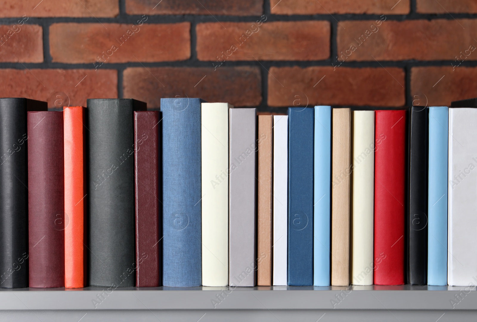 Photo of Many different hardcover books on grey table near brick wall