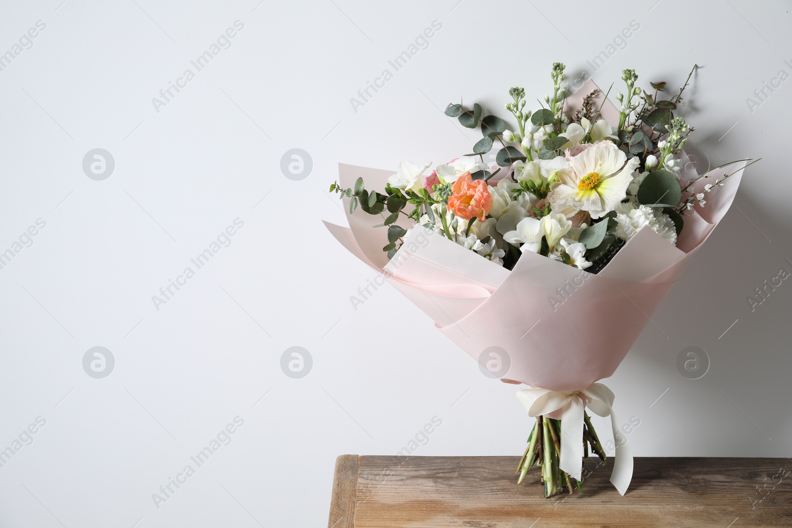 Photo of Bouquet of beautiful flowers on wooden table against white wall. Space for text