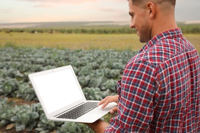 Man using laptop with blank screen in field, closeup. Agriculture technology