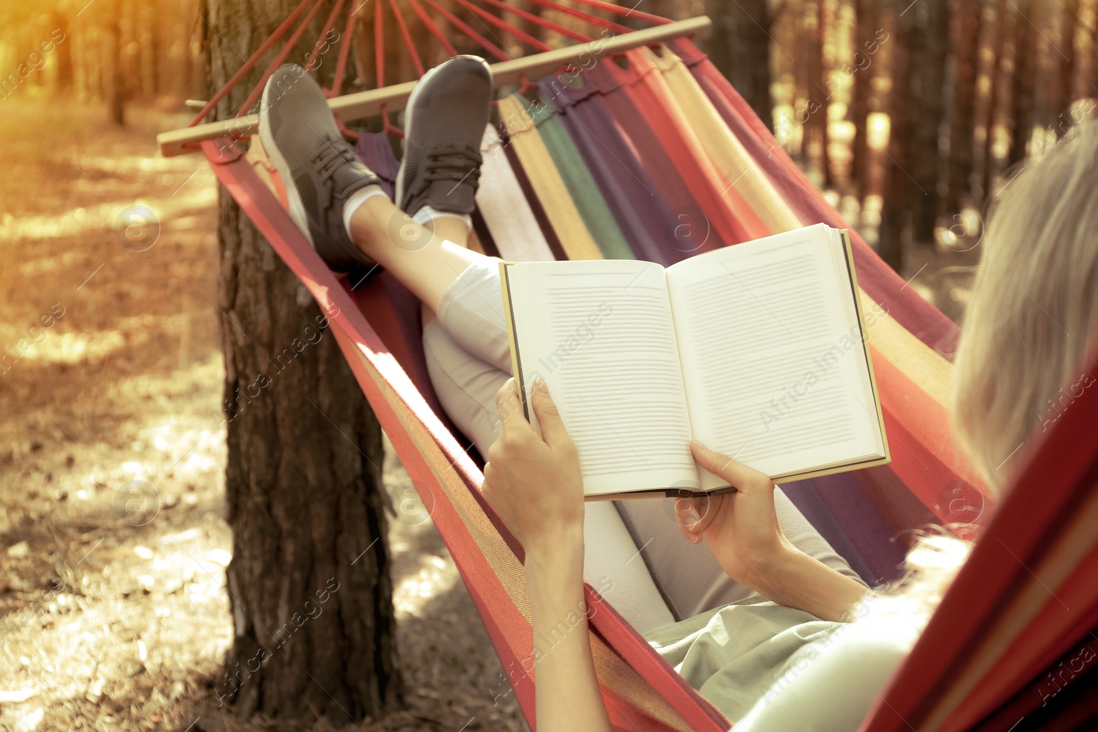 Photo of Woman with book relaxing in hammock outdoors on summer day, closeup