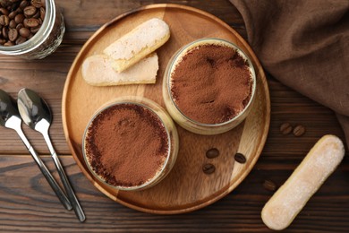 Photo of Delicious tiramisu in glasses served on wooden table, flat lay