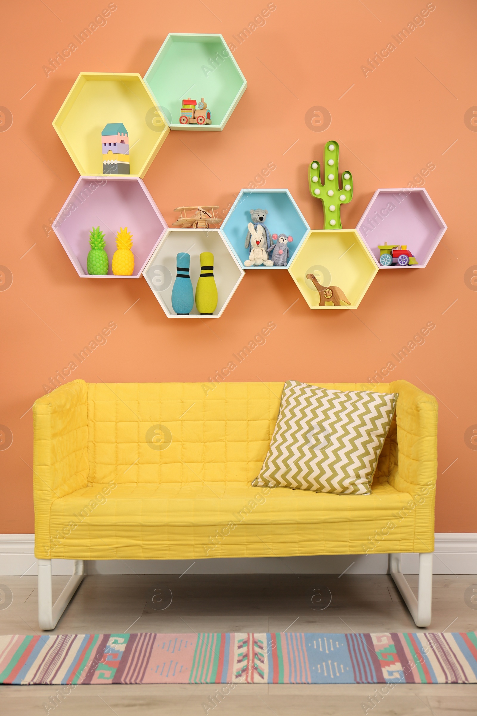 Photo of Sofa near orange wall with hexagon shaped shelves in room. Interior design
