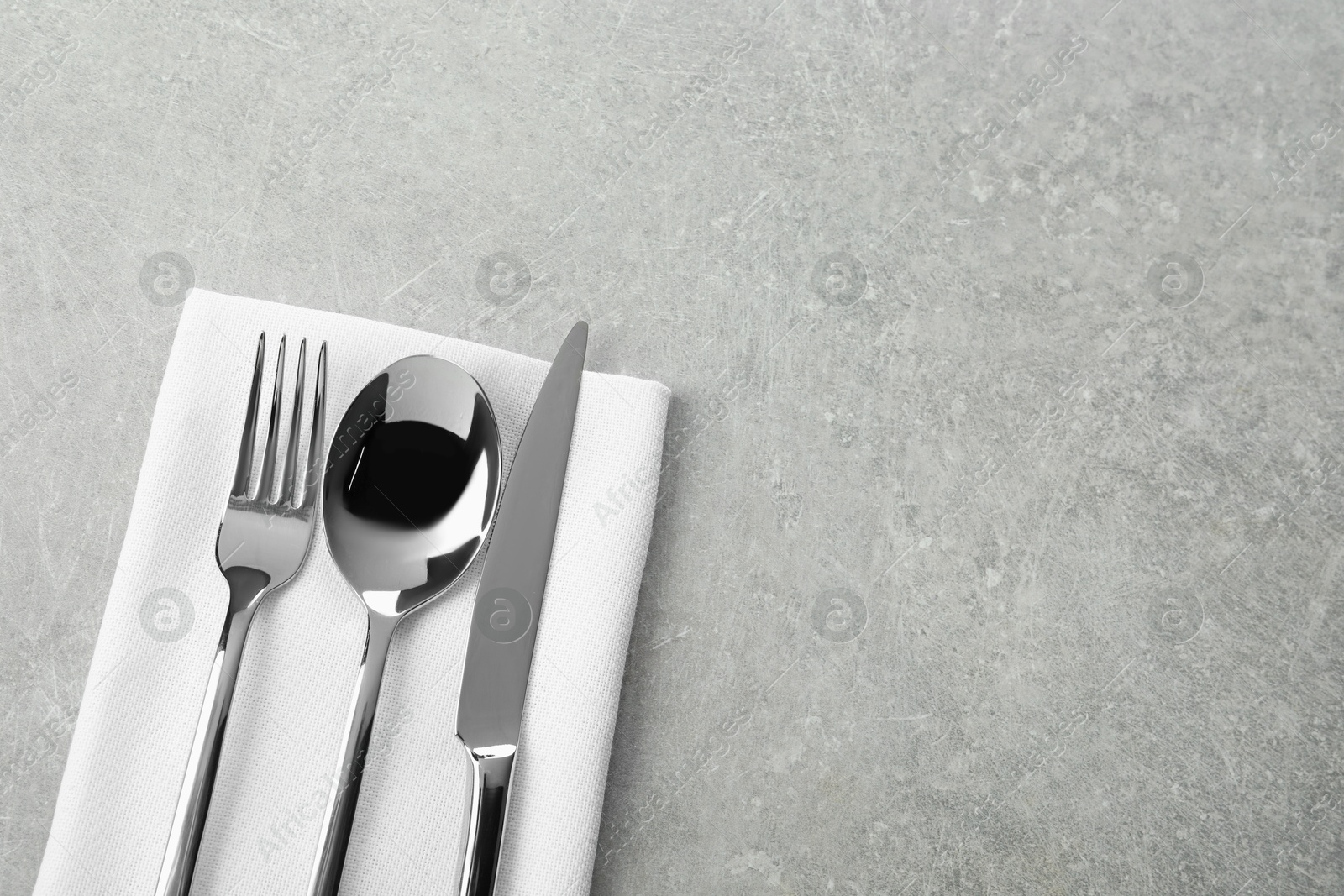 Photo of Stylish cutlery set and napkin on grey table, top view. Space for text