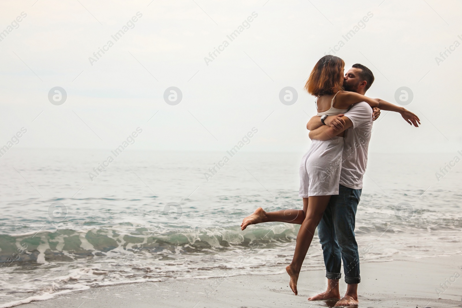 Photo of Young couple kissing on beach near sea. Space for text