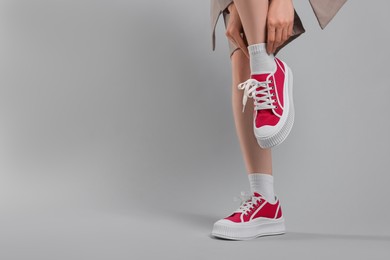 Photo of Woman posing in red classic old school sneakers on light gray background, closeup. Space for text