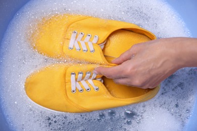 Photo of Woman washing sport shoes in plastic basin, top view