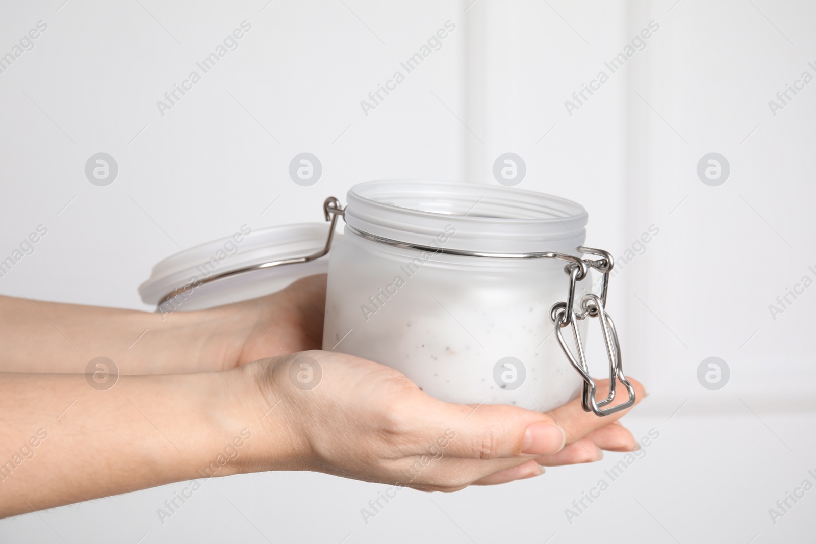 Photo of Woman holding jar of salt scrub on light background, closeup