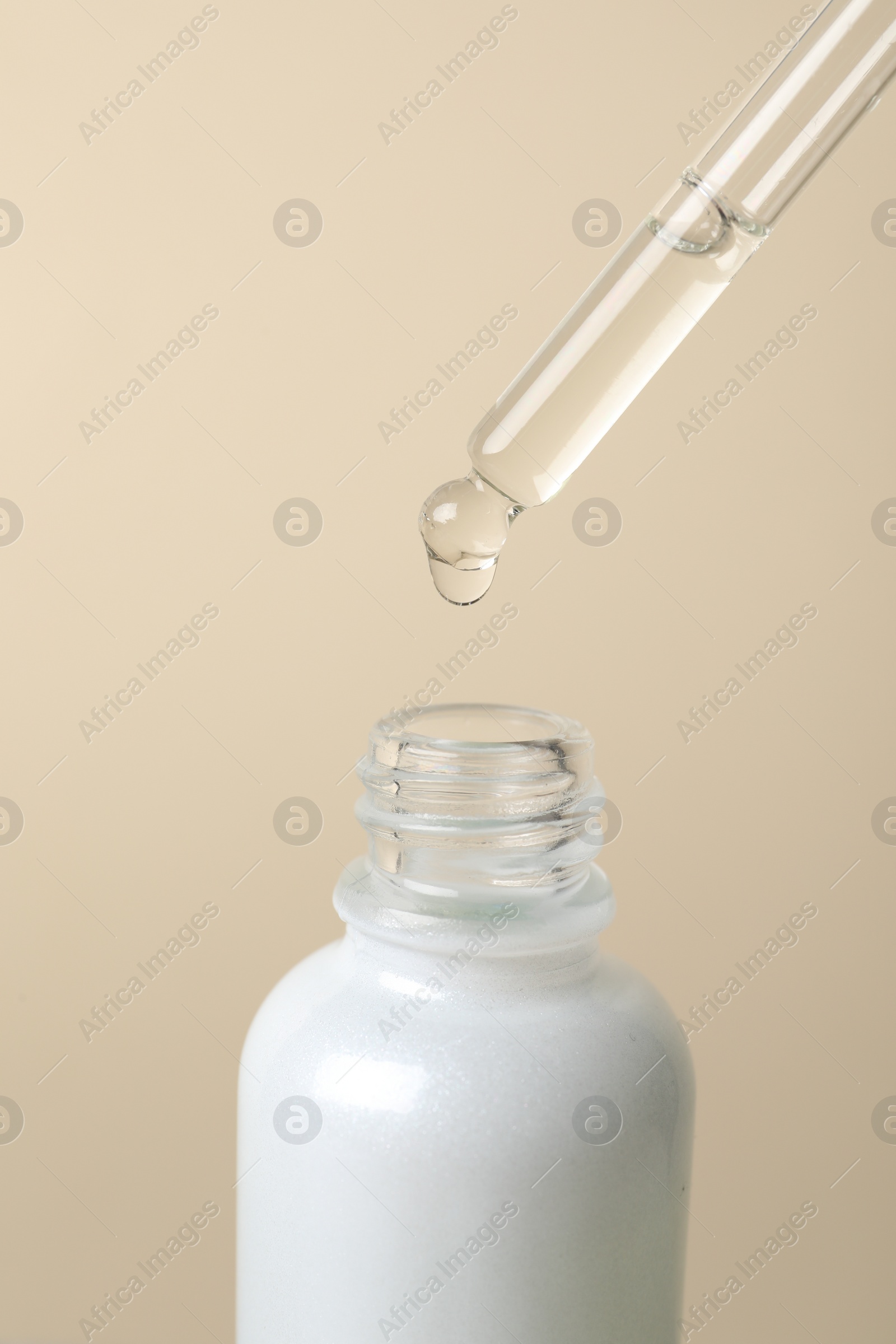 Photo of Dripping cosmetic serum from pipette into bottle on beige background