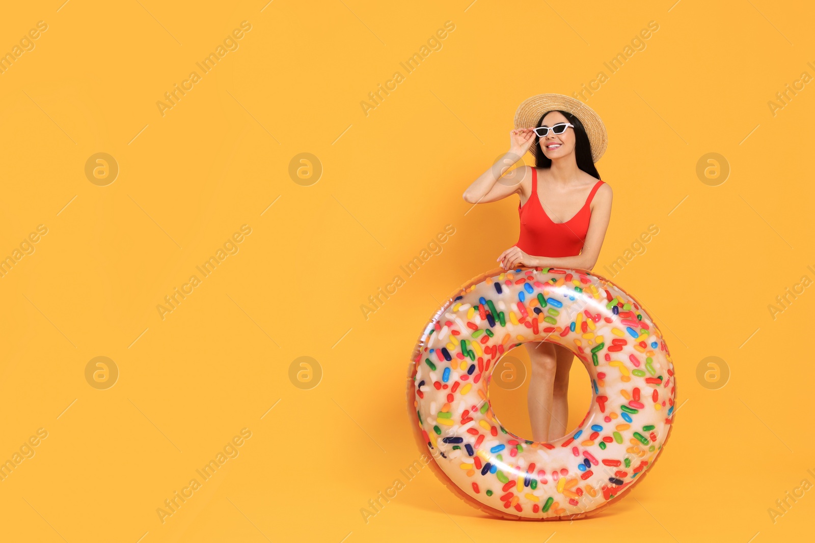 Photo of Happy young woman with beautiful suntan, hat, sunglasses and inflatable ring against orange background, space for text