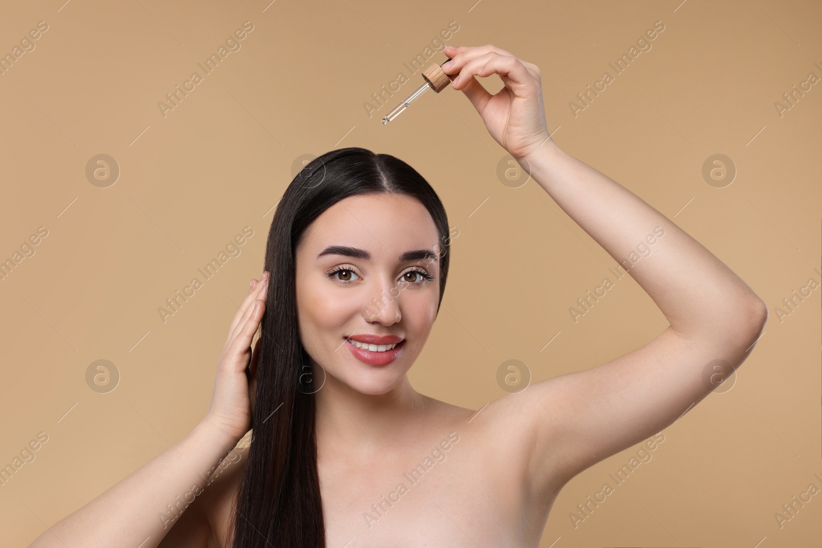 Photo of Happy woman applying essential oil onto hair roots on beige background