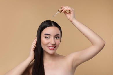 Happy woman applying essential oil onto hair roots on beige background