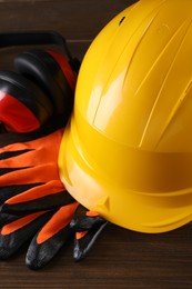 Hard hat, earmuffs and gloves on wooden table, closeup. Safety equipment