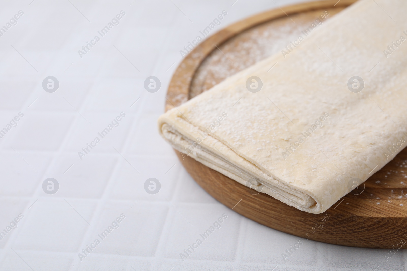 Photo of Raw puff pastry dough on white tiled table, closeup. Space for text