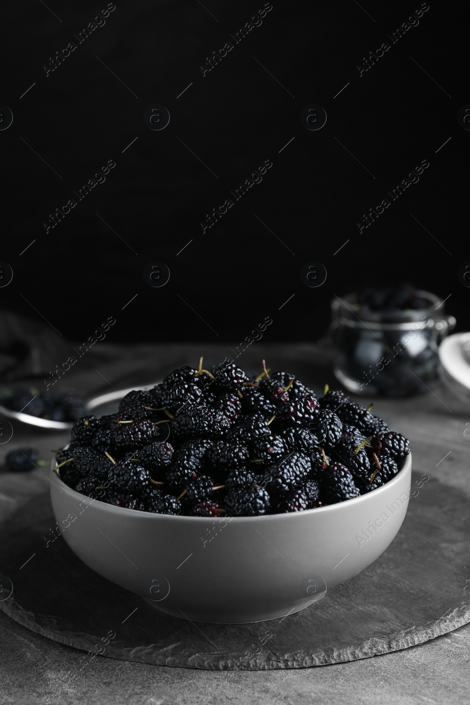 Photo of Bowl of delicious ripe black mulberries on grey table